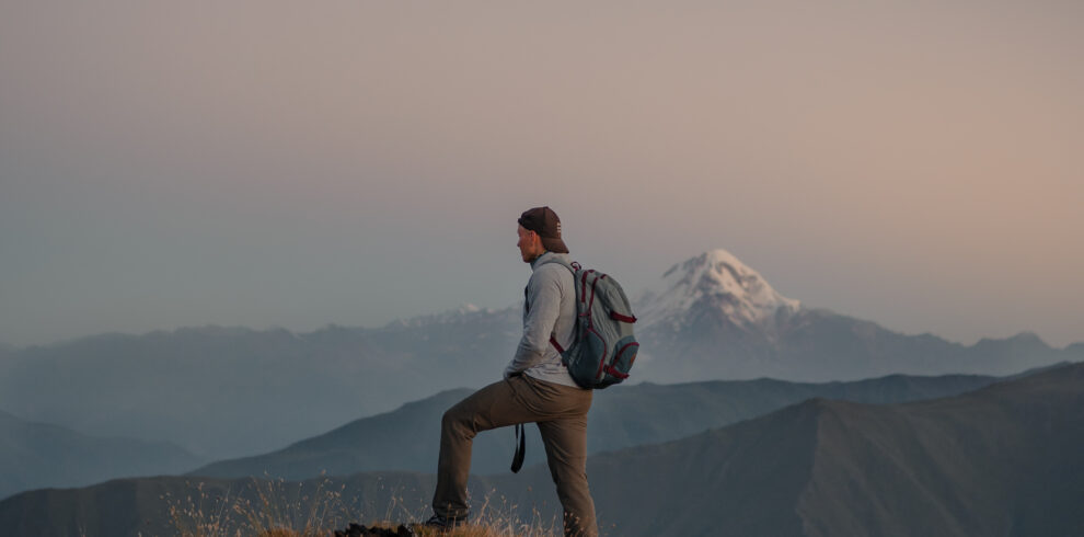 Young Caucasian male hiker standing at the top of a grassy mountain and admiring the foggy nature